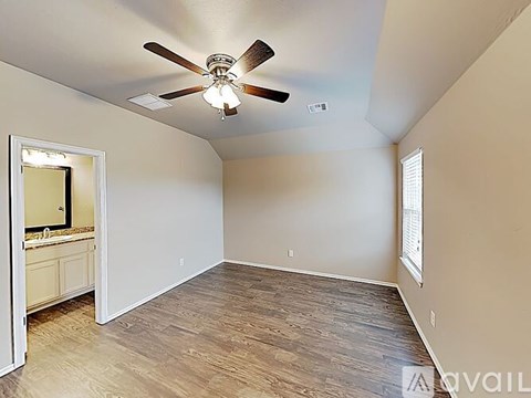 A room with a ceiling fan and light fixture, wooden flooring, and a window with blinds.