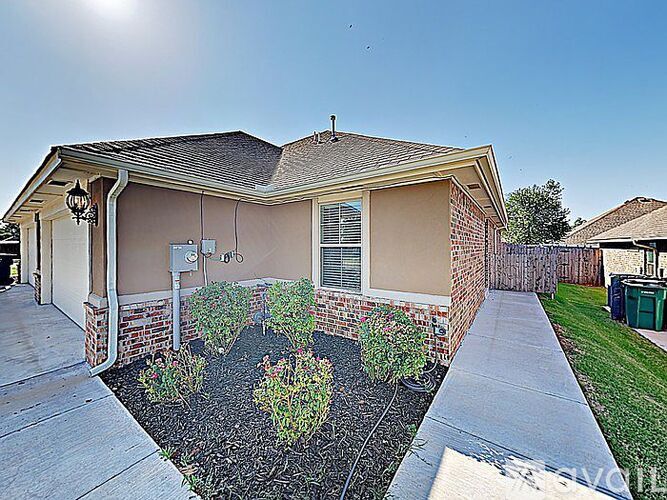 A house with a brown roof and a small front yard with plants.