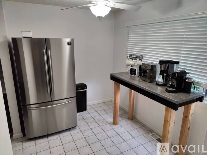 A kitchen with a stainless steel refrigerator and a black countertop with a coffee maker and other items on it.