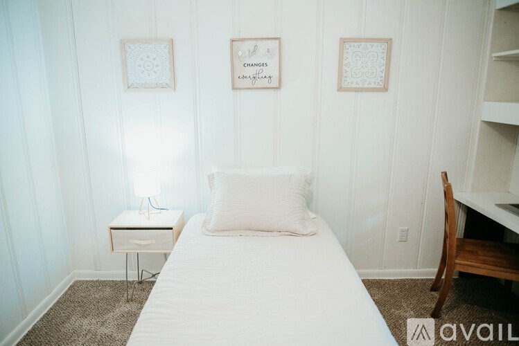 A white bedroom with a bed, nightstand, and two pictures on the wall.