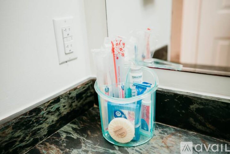 A clear cup on a marble countertop contains toothbrushes and toothpaste.