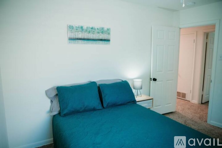 A bedroom with a bed, two pillows, a nightstand with a lamp, and a painting on the wall.