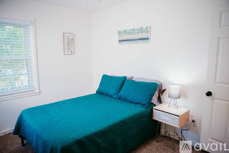 A bedroom with a blue bedspread and a white nightstand with a lamp.