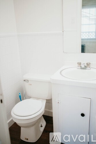 A white toilet with a toothbrush on the side and a sink with a mirror above it.