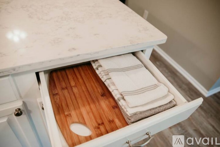 A white cabinet with a drawer open, revealing a wooden cutting board and towels.