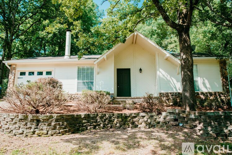 A white house with a green door and windows is surrounded by trees.
