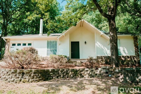 A white house with a green door and windows is surrounded by trees.