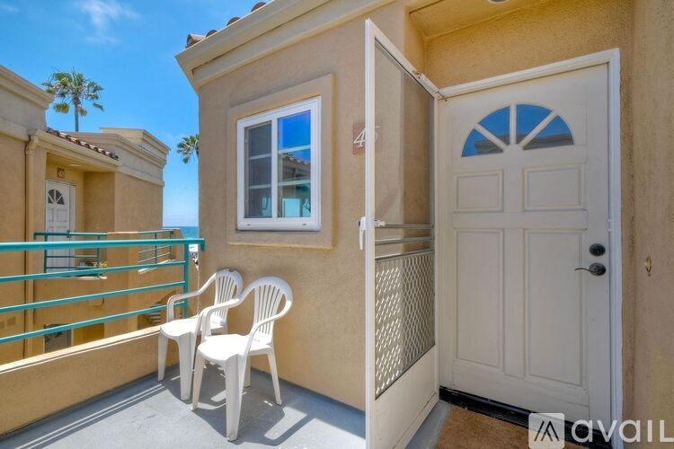 A balcony with a white chair overlooks a beach with palm trees.