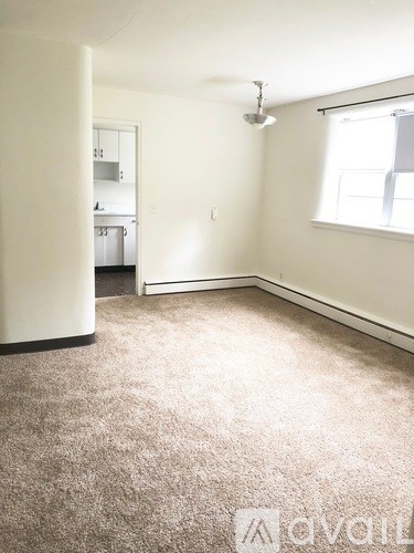 A carpeted room with a window and a door leading to another room.