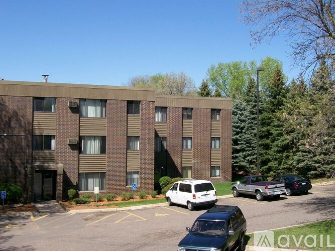 A parking lot in front of a brick apartment building with cars parked.