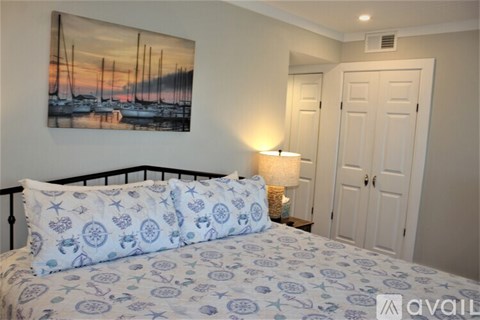 A bedroom with a bed, a painting on the wall, and a lamp on the side table.