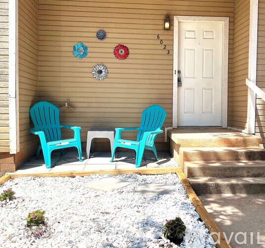 Two blue chairs are on a porch with a white door.