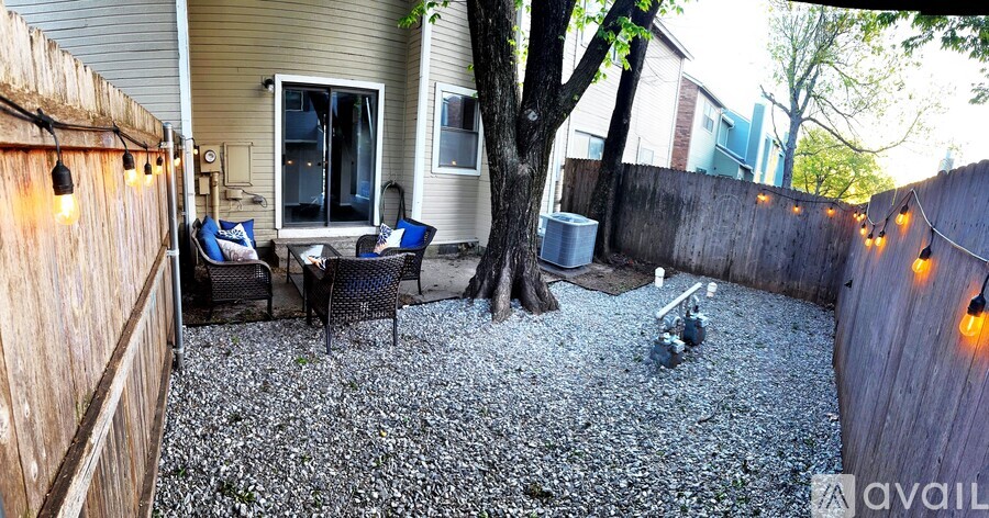A backyard with a gravel patio, a tree, and a fence.