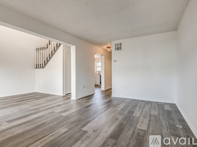 A spacious room with wooden flooring and a staircase on the left side.