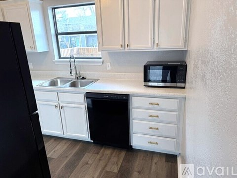 A black refrigerator stands next to a white sink in a kitchen.