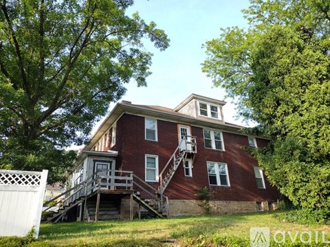 A red brick house with a white fence and a tree in front.