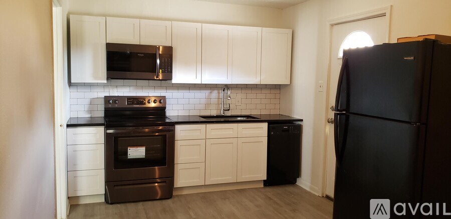 A black refrigerator stands in a kitchen with white cabinets and a black countertop.