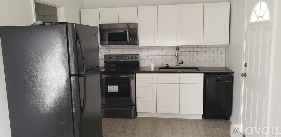 A black refrigerator stands in a kitchen with white cabinets and a black dishwasher.