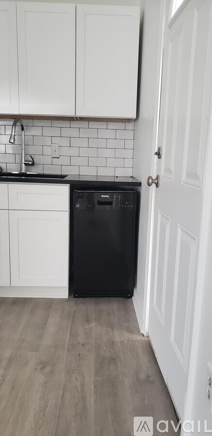 A black trash bin sits in a kitchen next to a white door.