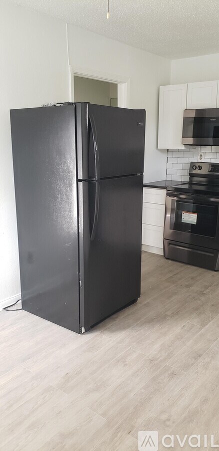 A black refrigerator in a kitchen with wooden flooring.