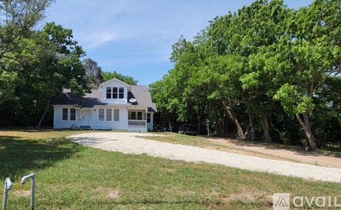 A white house with a black roof is surrounded by green trees.