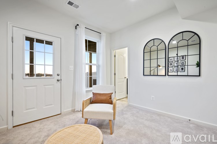 A room with a white door, a window with white curtains, a wooden chair, and a wall with two framed pictures.