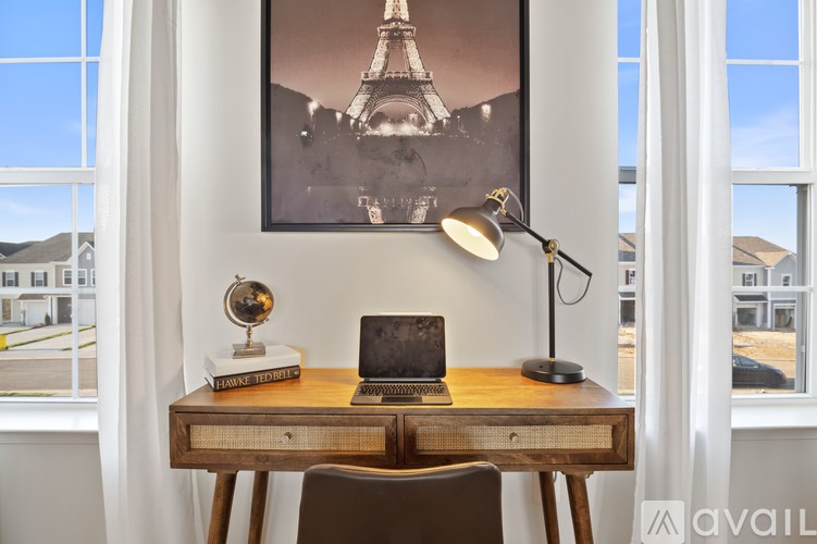 A desk with a laptop, lamp, and globe in front of a framed picture of the Eiffel Tower.