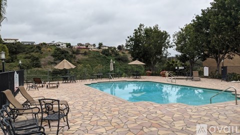 A pool surrounded by chairs and trees with a hill in the background.
