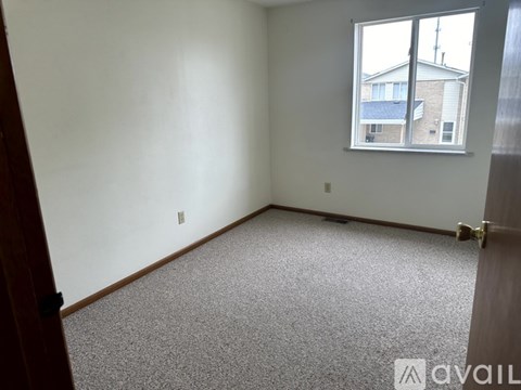A room with a carpeted floor and a window showing a building outside.