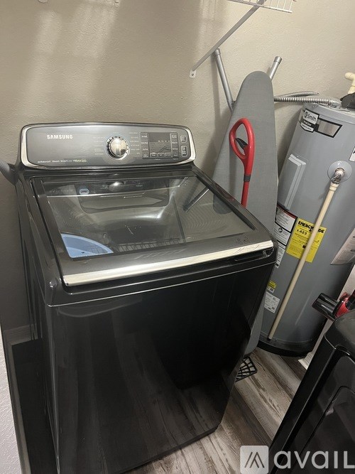A black Samsung washing machine with a red hose and a grey dryer in a laundry room.