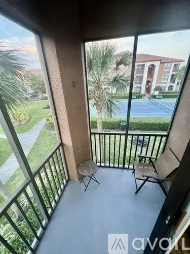 A balcony with a table and two chairs overlooks a tennis court.