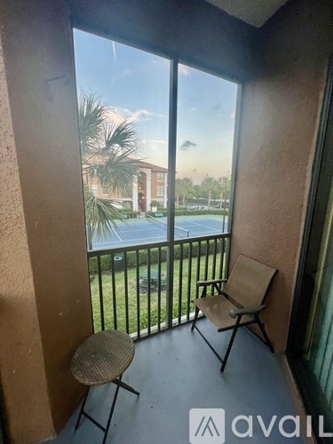 A balcony with a chair and a table overlooking a pool and buildings.