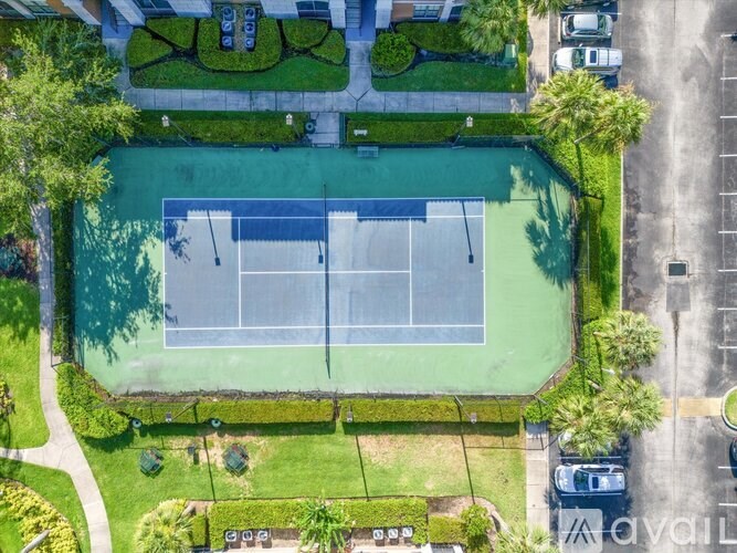 An aerial view of a tennis court surrounded by greenery and a parking lot.