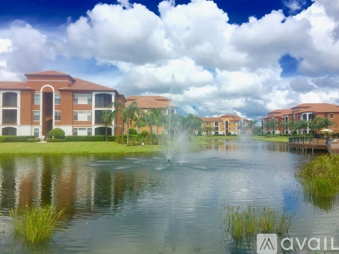 A fountain in the middle of a pond in front of apartment buildings.