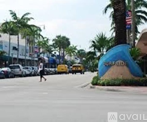 A person is walking on a street with palm trees and a Surfside sign.