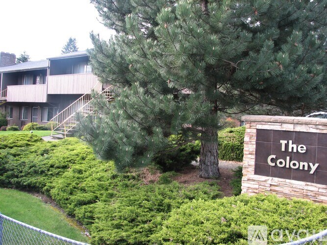 A sign that says "The Colony" stands in front of a building and trees.