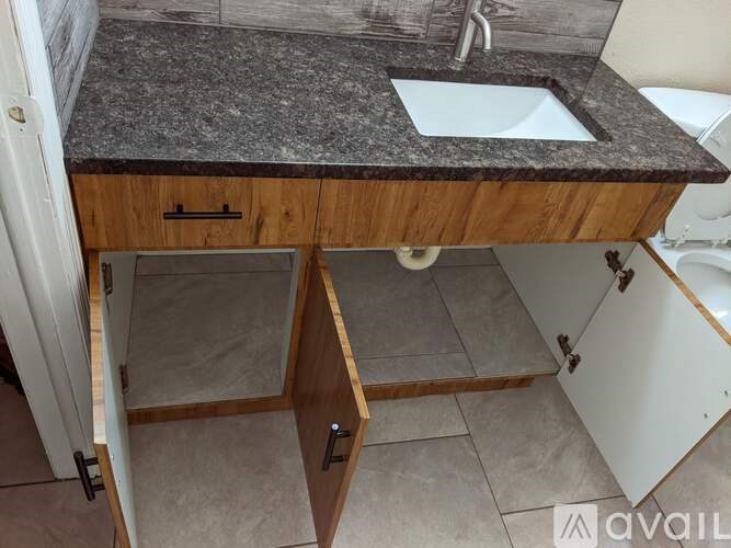 A bathroom sink with a granite countertop and wooden cabinetry.