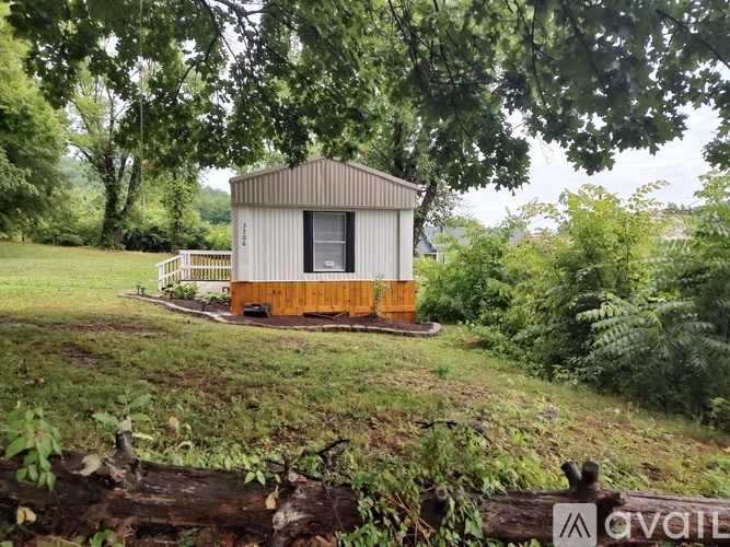 A small cabin sits in a grassy field with trees in the background.