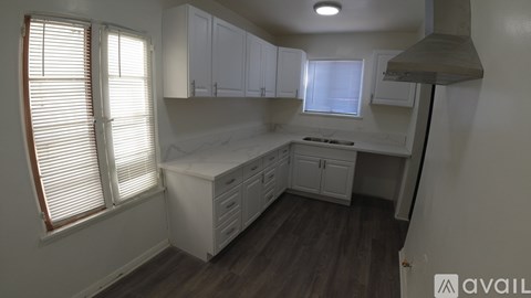 A kitchen with white cabinets and a window with blinds.