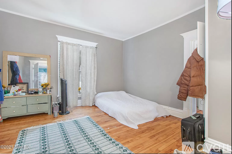 A bedroom with a white bed and a green rug.