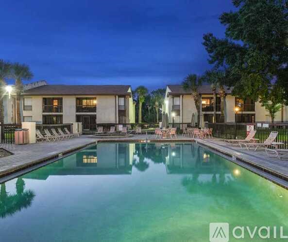 A pool area with lounge chairs and a building in the background at dusk.