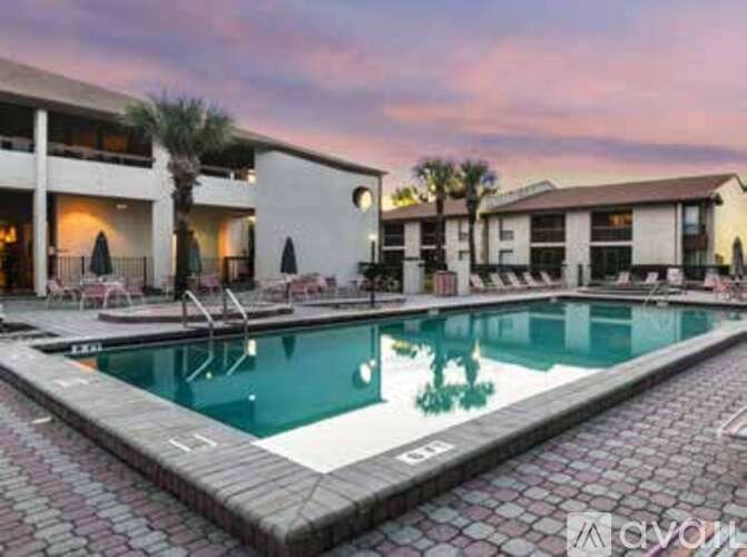 A large outdoor swimming pool surrounded by a brick patio and lounge chairs.