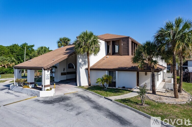 A house with a brown roof and white walls is surrounded by palm trees.