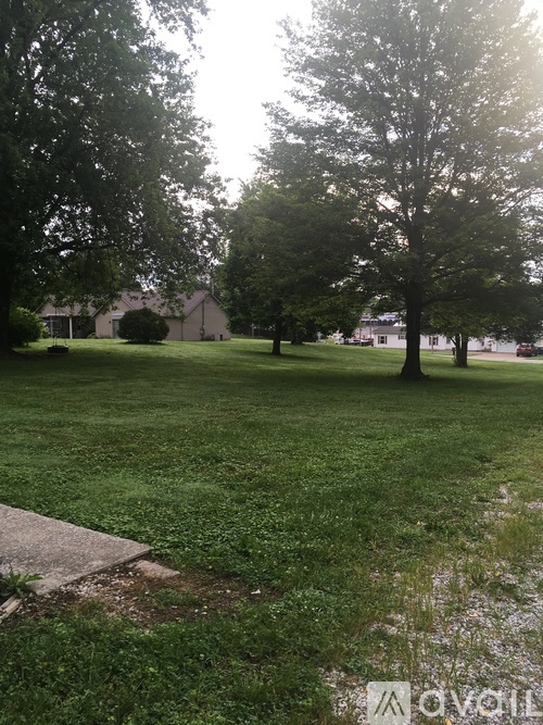 A grassy field with trees and a house in the background.