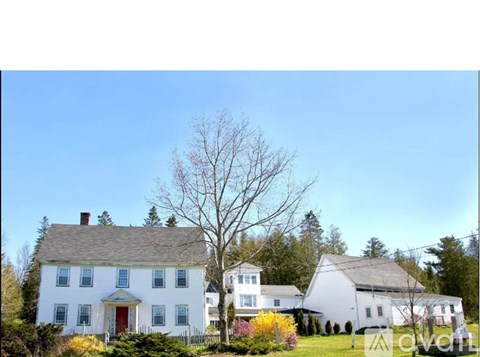 A white house with a red door is surrounded by trees and bushes.