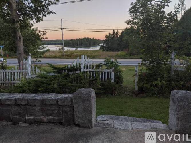 A stone wall with a white fence in the foreground and a body of water in the distance.
