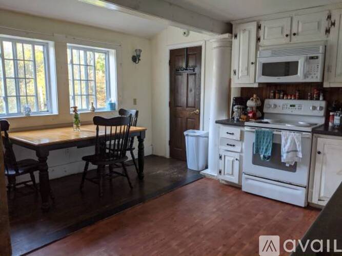 A kitchen with a wooden table and chairs, a white stove, and a window with a view of trees.