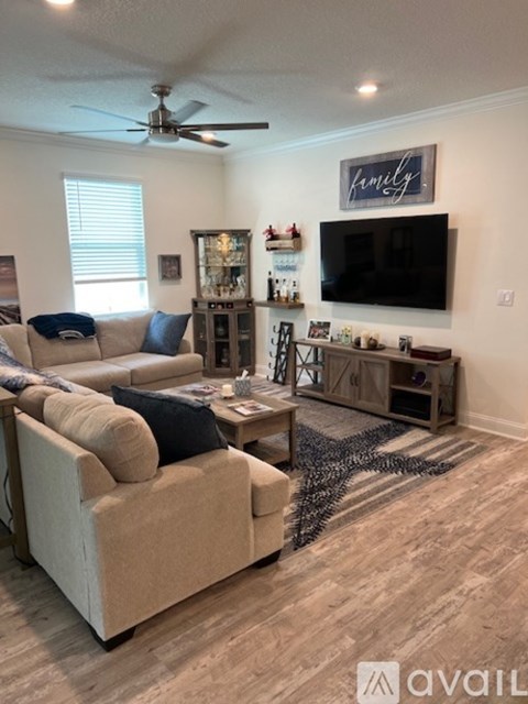 A living room with a beige couch and a flat screen TV mounted on the wall.