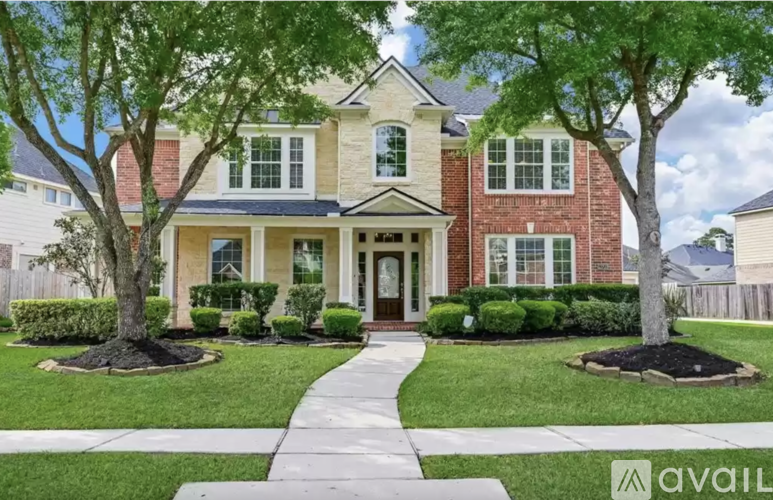 A house with a brick facade and a white door is surrounded by greenery.