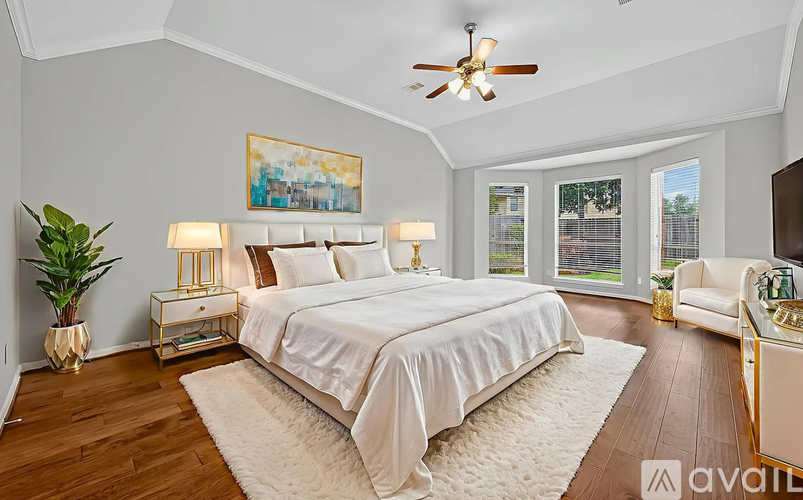 A bedroom with a large bed, a ceiling fan, and a painting on the wall.